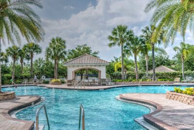 Huge outdoor pool with pool features for luxury properties surrounded by palm trees and deck chairs 
