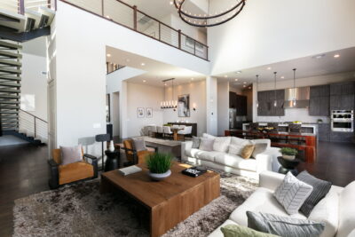 A spacious, modern open-concept living area with a high ceiling in guard-gated Summerlin, featuring two sofas, armchairs, a large wooden coffee table, with kitchen and dining spaces visible. Contemporary décor and neutral tones throughout.