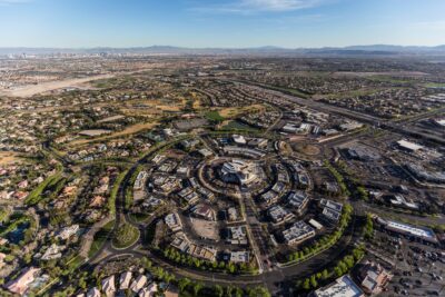 Aerial view of Summerlin, a sought-after place to live featuring circular residential and commercial developments, surrounded by roads and greenery, with an expansive cityscape and distant mountains in the background.