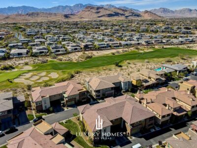Aerial view of a luxury neighborhood in Las Vegas with houses, a green golf course, and mountains in the background under a clear blue sky.
